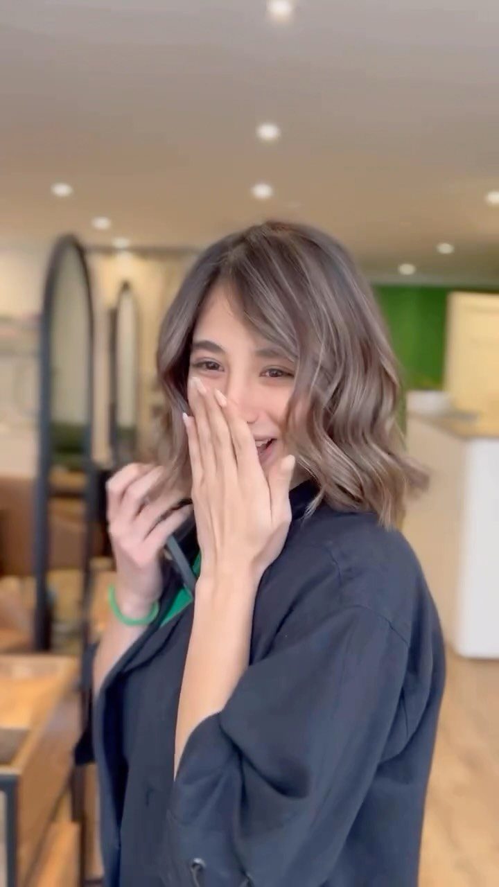 Woman showing a wavy ash-brown bob with side-swept bangs in a salon