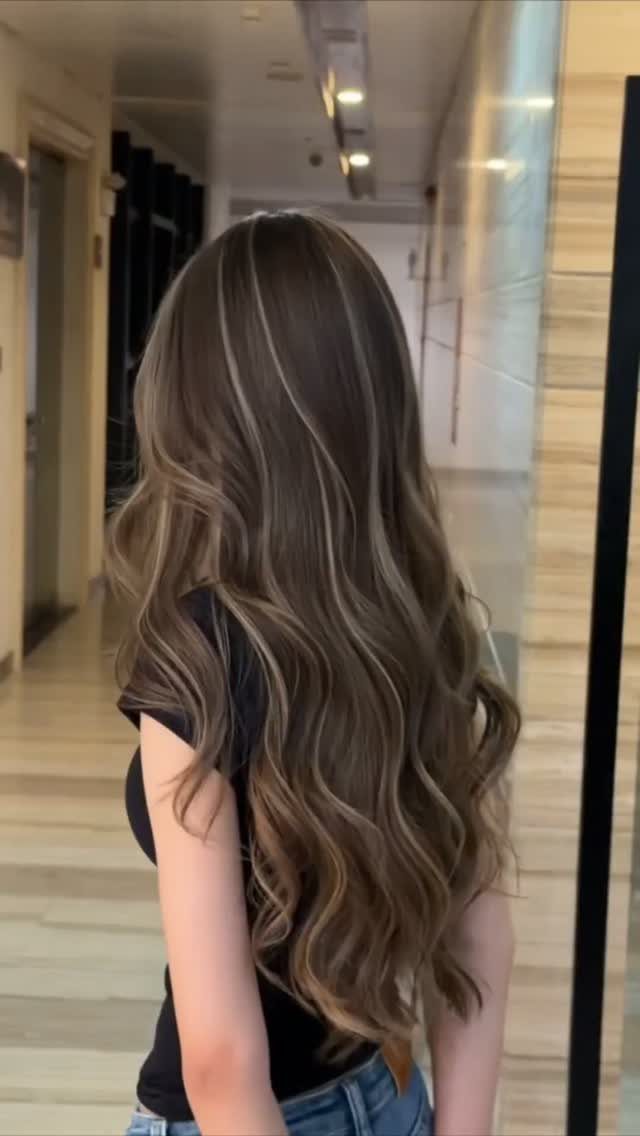 Long ash-brown waves with fine lighter highlights fall down a person's back.