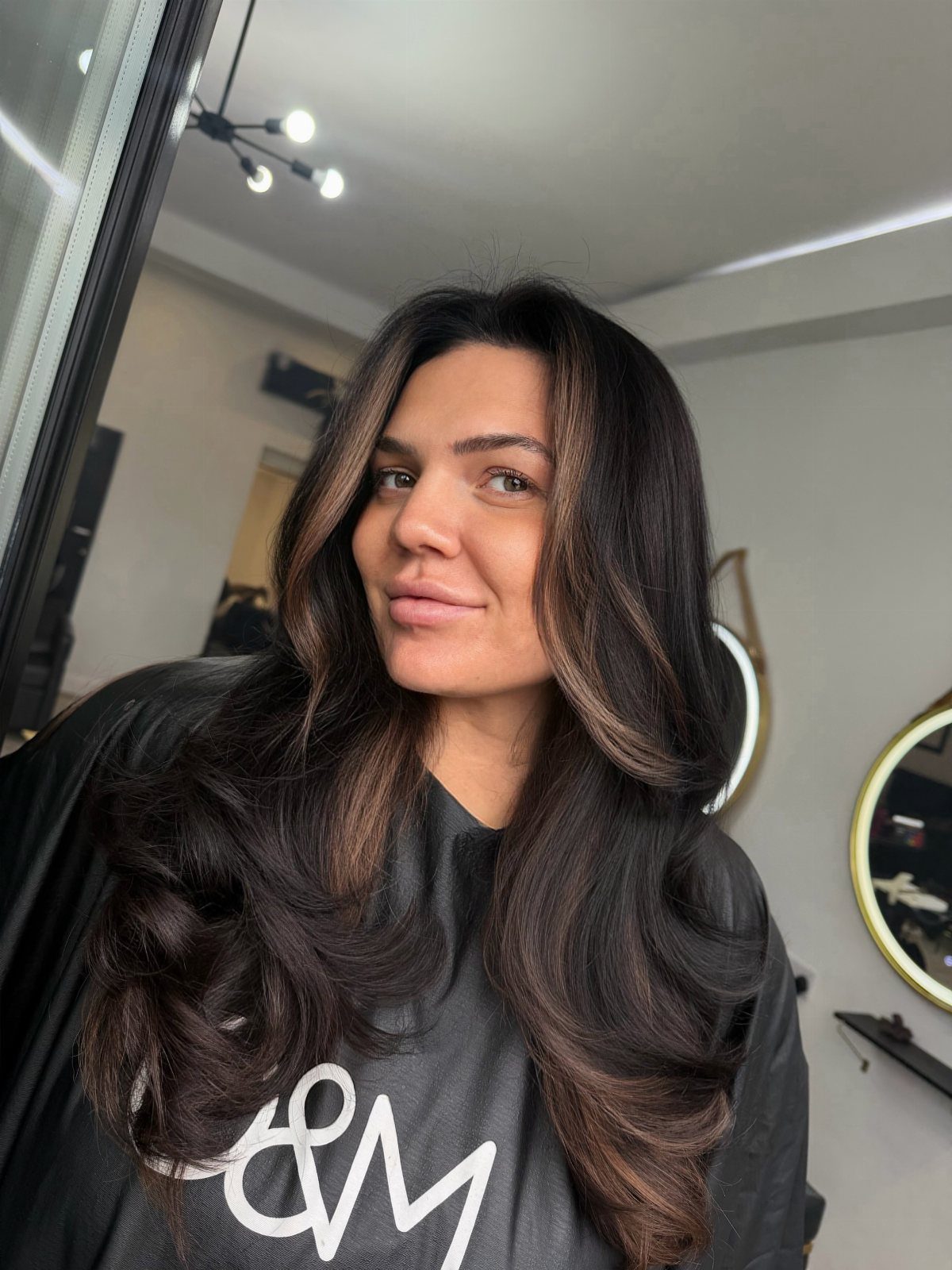 Woman with long dark hair and soft bronze balayage curled through the ends