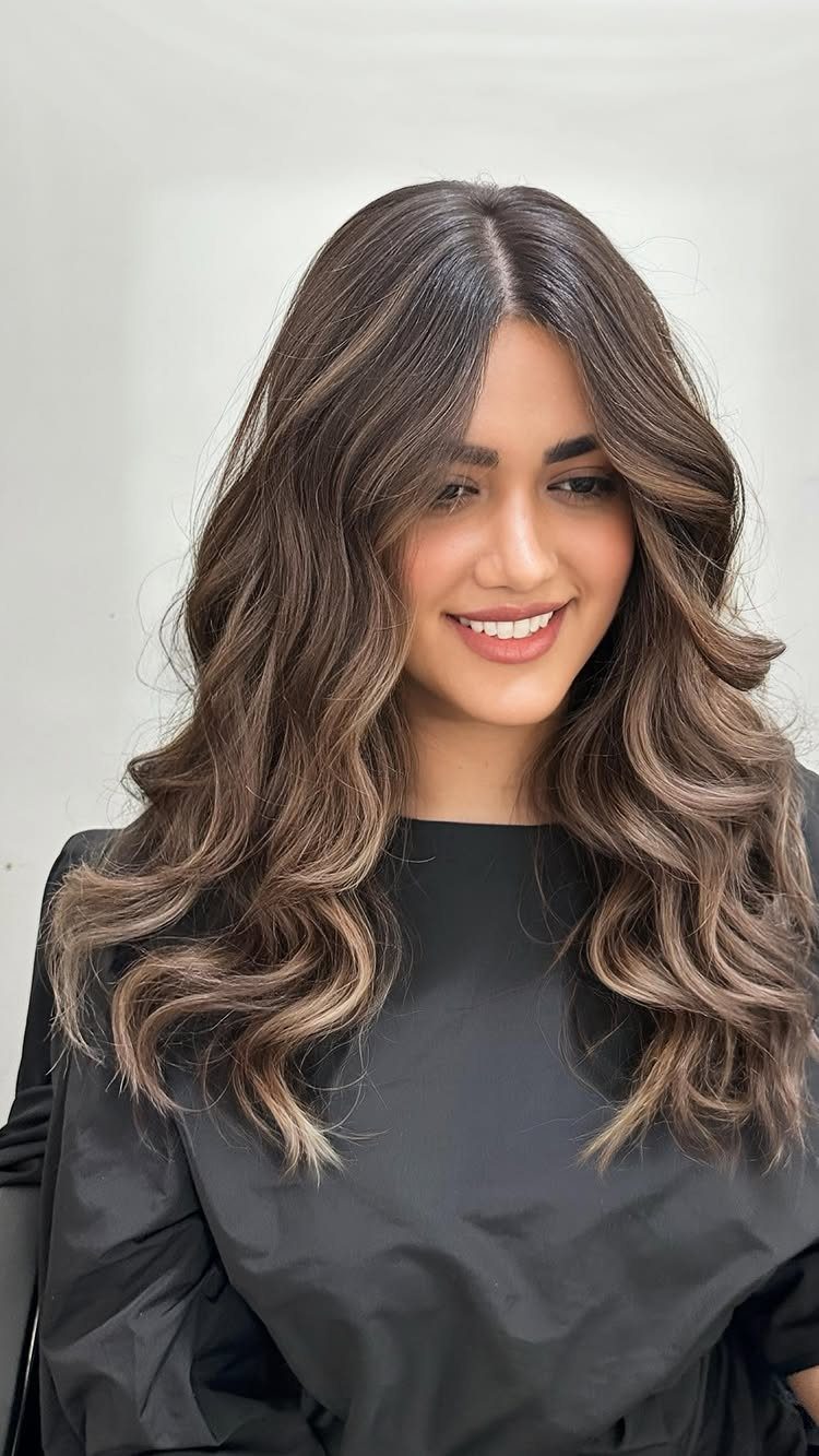 Woman with long dark brown waves and lighter chocolate balayage highlights
