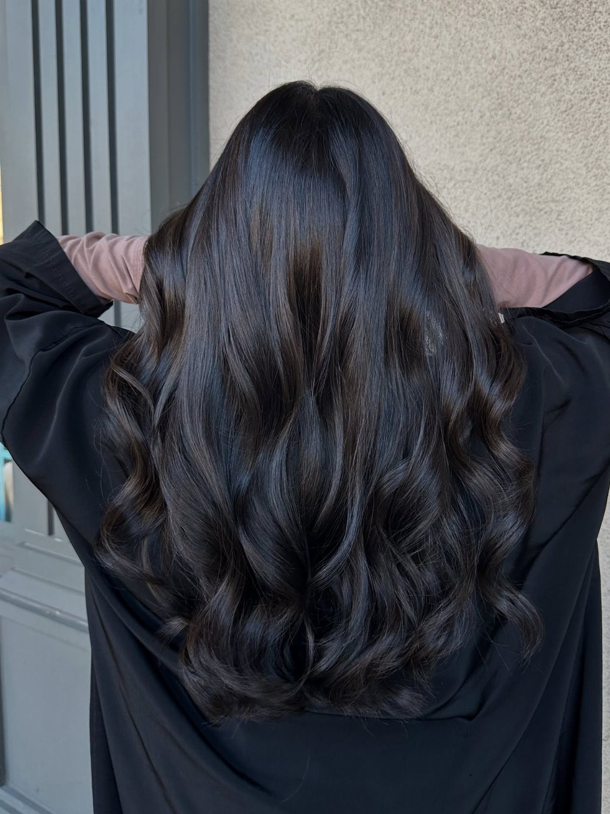 Long dark ash brown hair falls in glossy waves over a black salon cape.