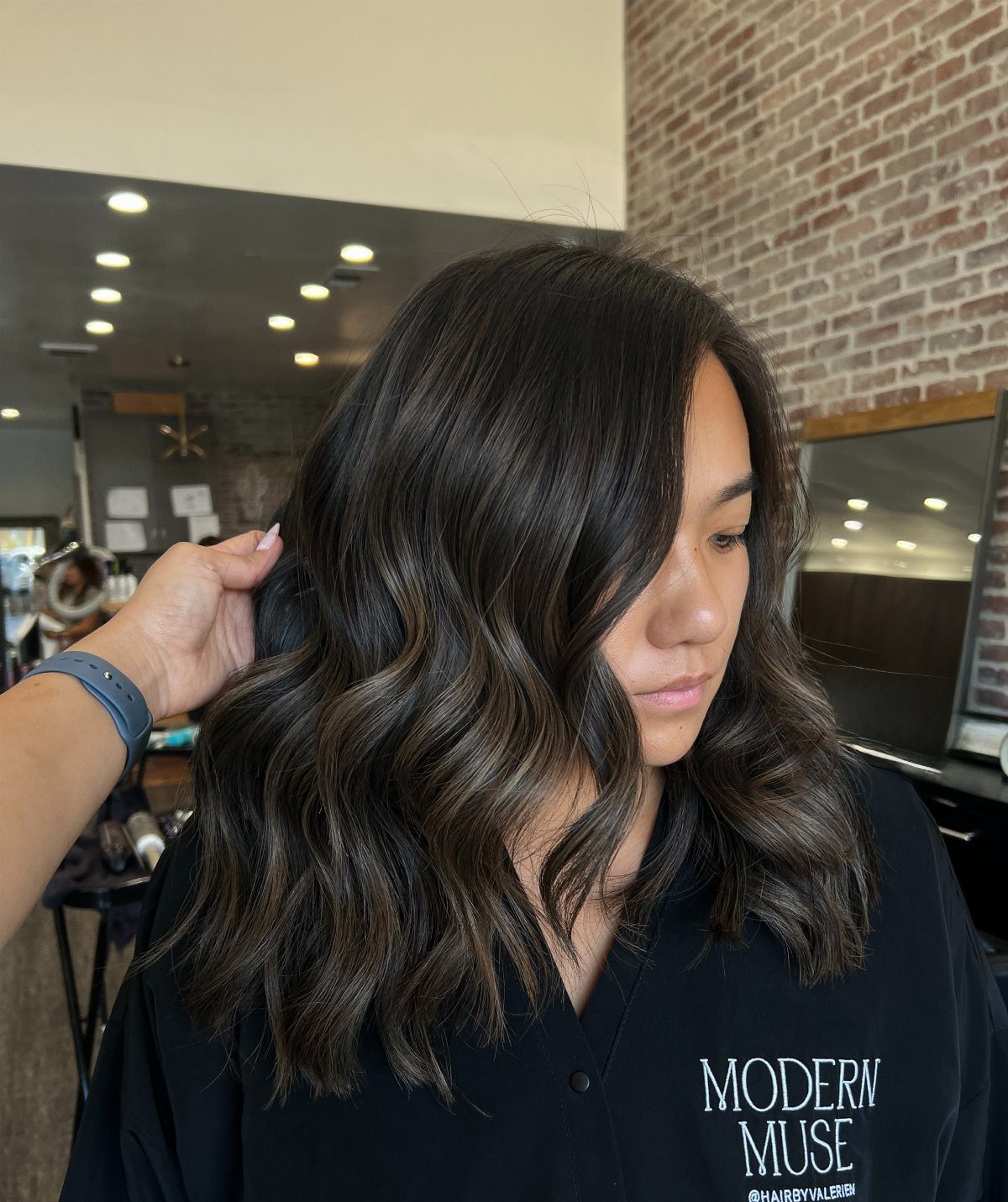 Woman displaying dark ash brown waves with lighter face-framing balayage in a salon