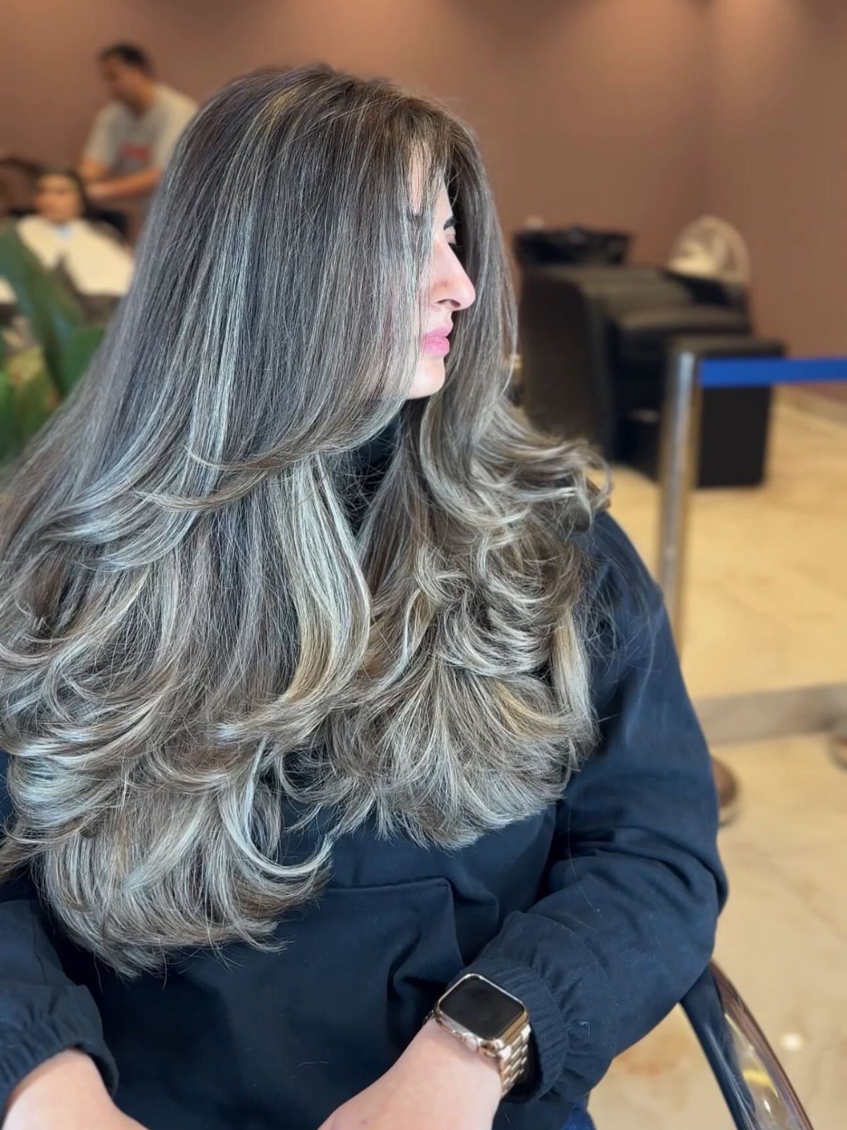 Long layered gray-brown hair with dark roots styled in loose curls