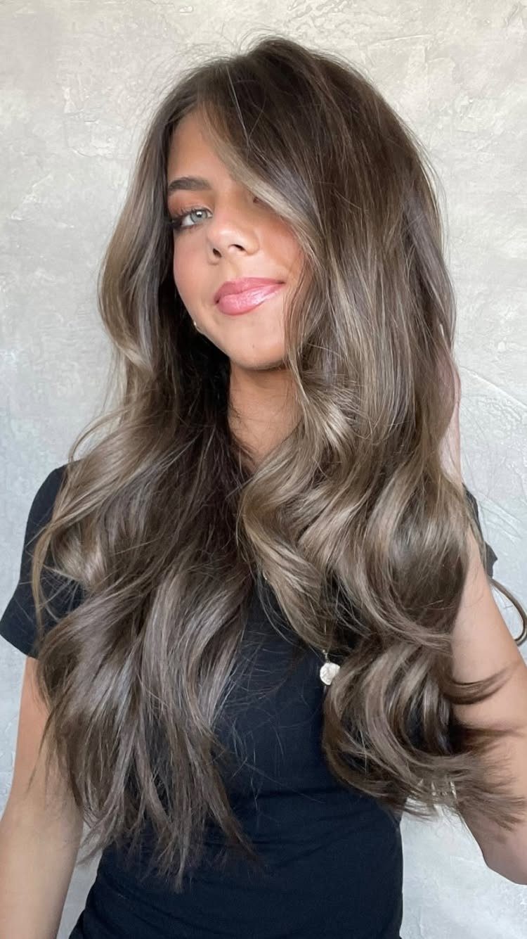 Woman with long brunette waves and cool silvery highlights against a pale wall