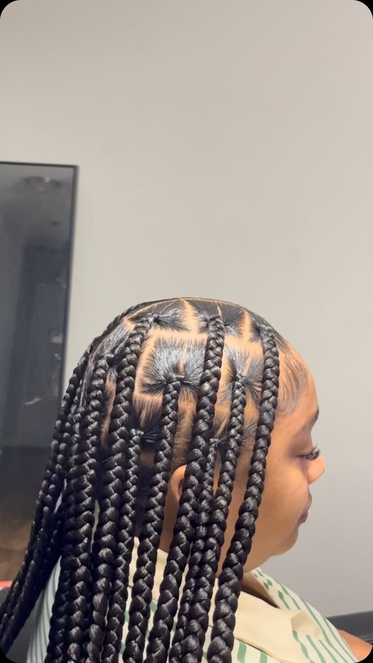 Long black box braids fall from square scalp sections on a seated person.