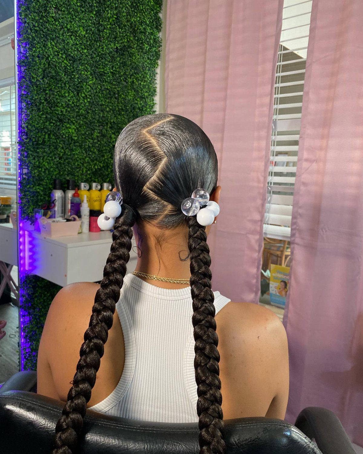 Two long black braids hang from a center part, decorated with white flower clips