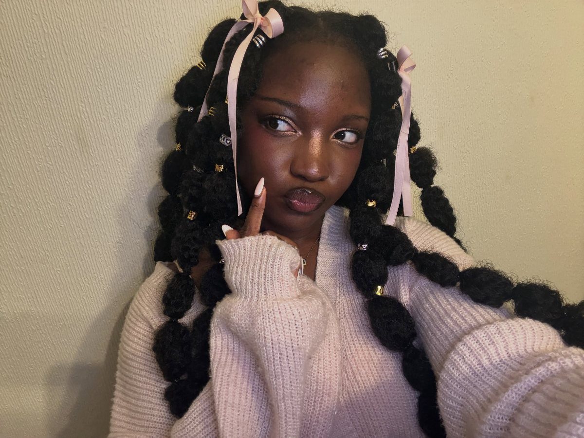 Woman with thick black braids adorned with pale pink ribbons and gold cuffs