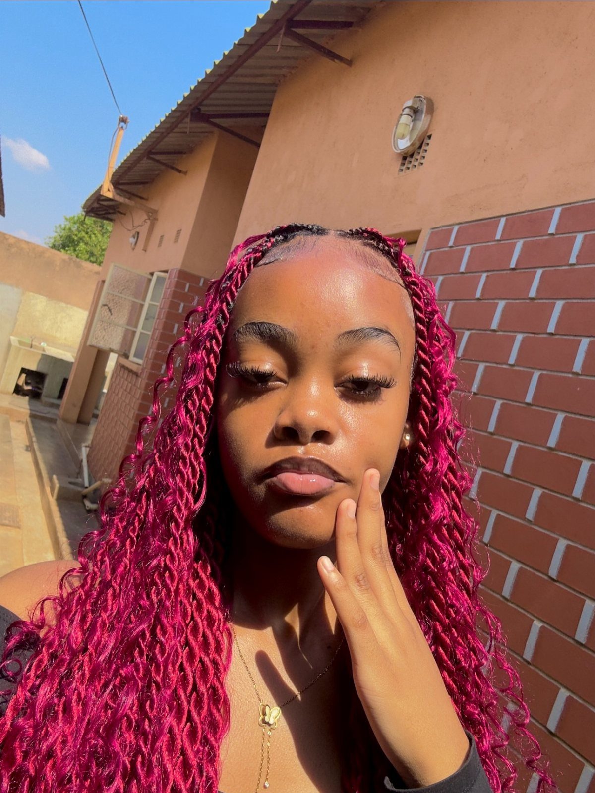 Woman with long burgundy braids takes a sunny outdoor selfie