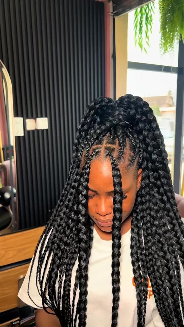 Long black Ghana braids cascade over a person’s white top