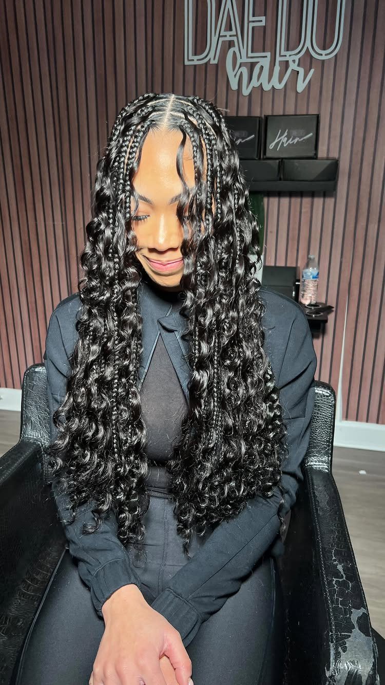 Woman displaying long black knotless braids with curly ends in a salon chair