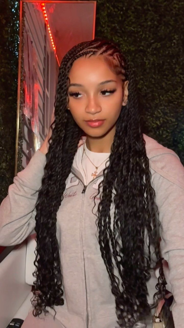 Woman with long black side-swept cornrows and curly braided extensions wearing a gray top