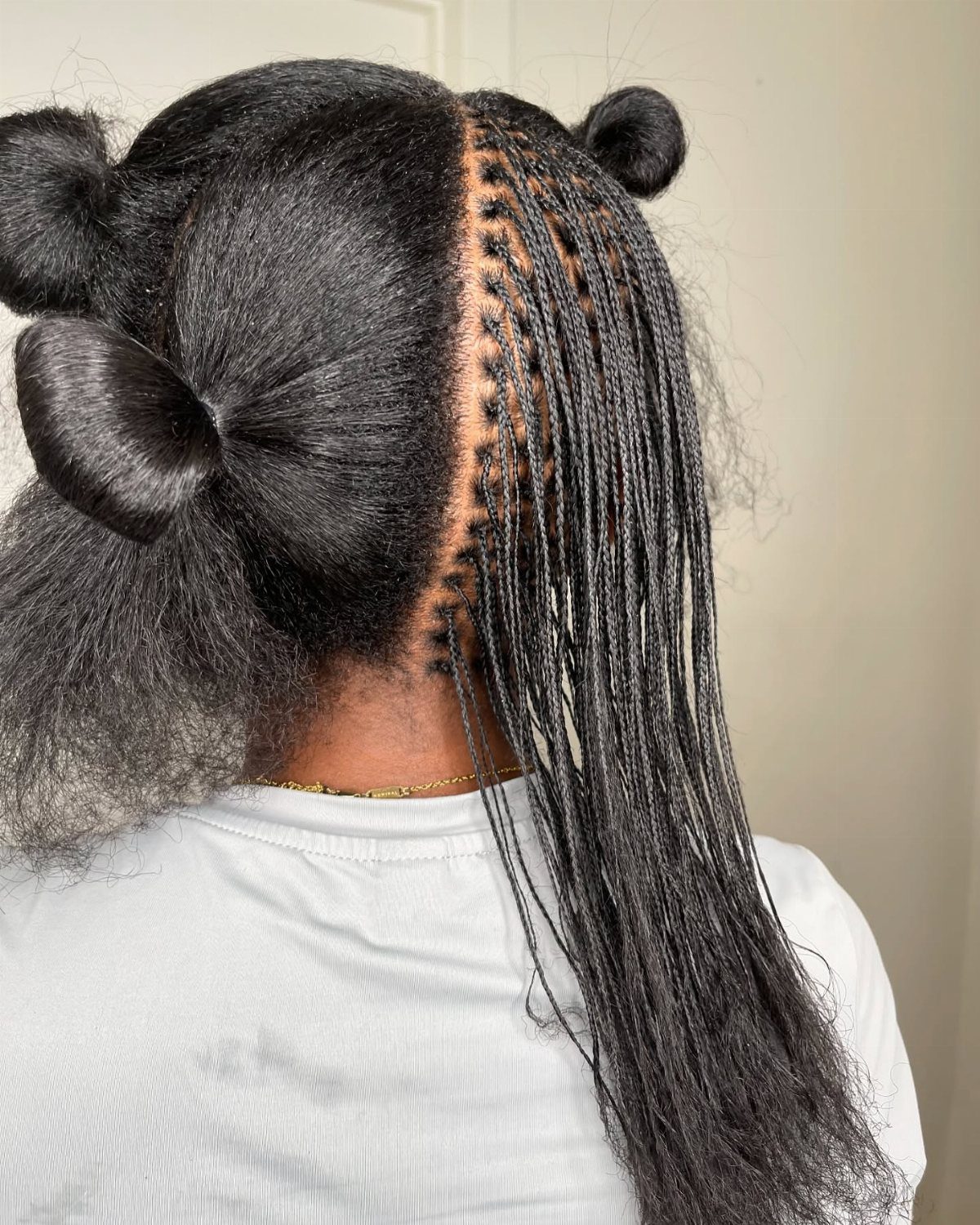 Fine black micro braids hang beside sectioned hair gathered into buns