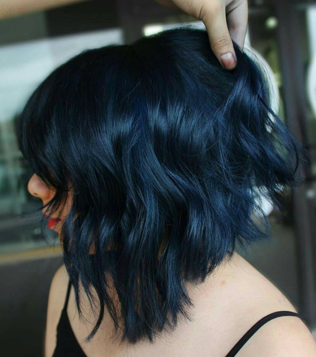 Wavy shoulder-length blue-black hair lifted by a hand outdoors