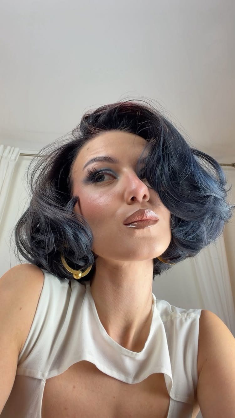 Woman with a wavy dark blue-black bob and gold hoop earrings