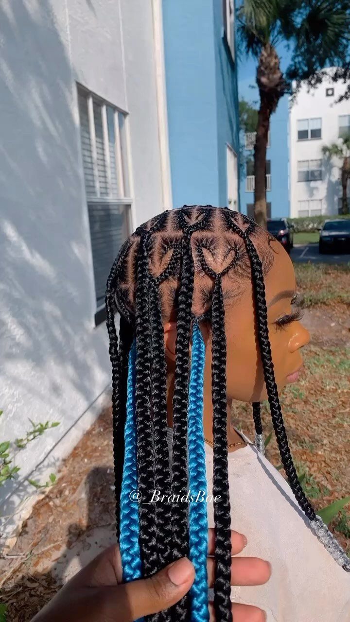 Long black braids with vivid blue strands hang beside a white building