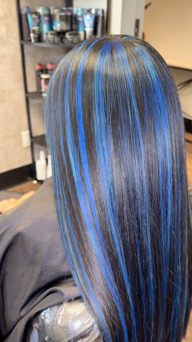Long dark hair with bright blue highlights styled straight in a salon