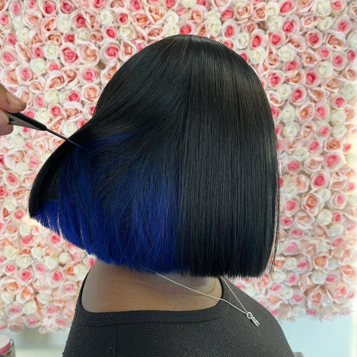 Black bob with vivid blue sections underneath, shown against a rose-covered wall