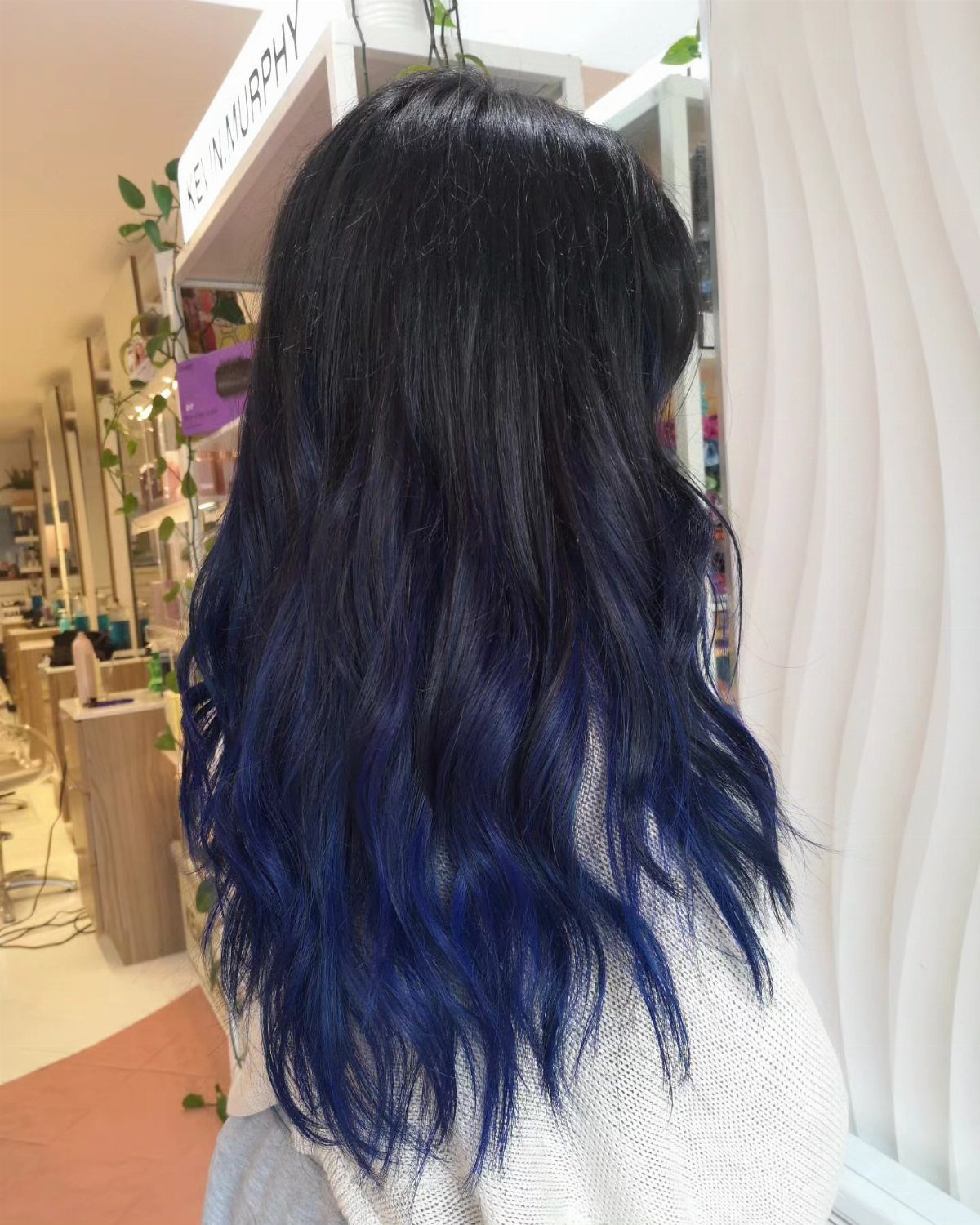 Long wavy black hair fading into deep blue ends in a salon