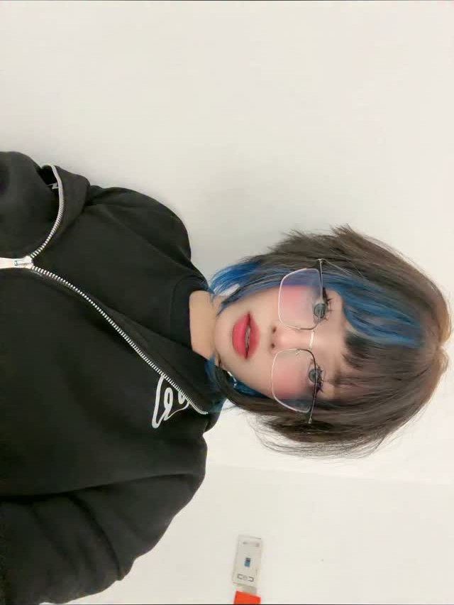 Short brown hair with bright blue face-framing streaks, glasses, and black sweatshirt