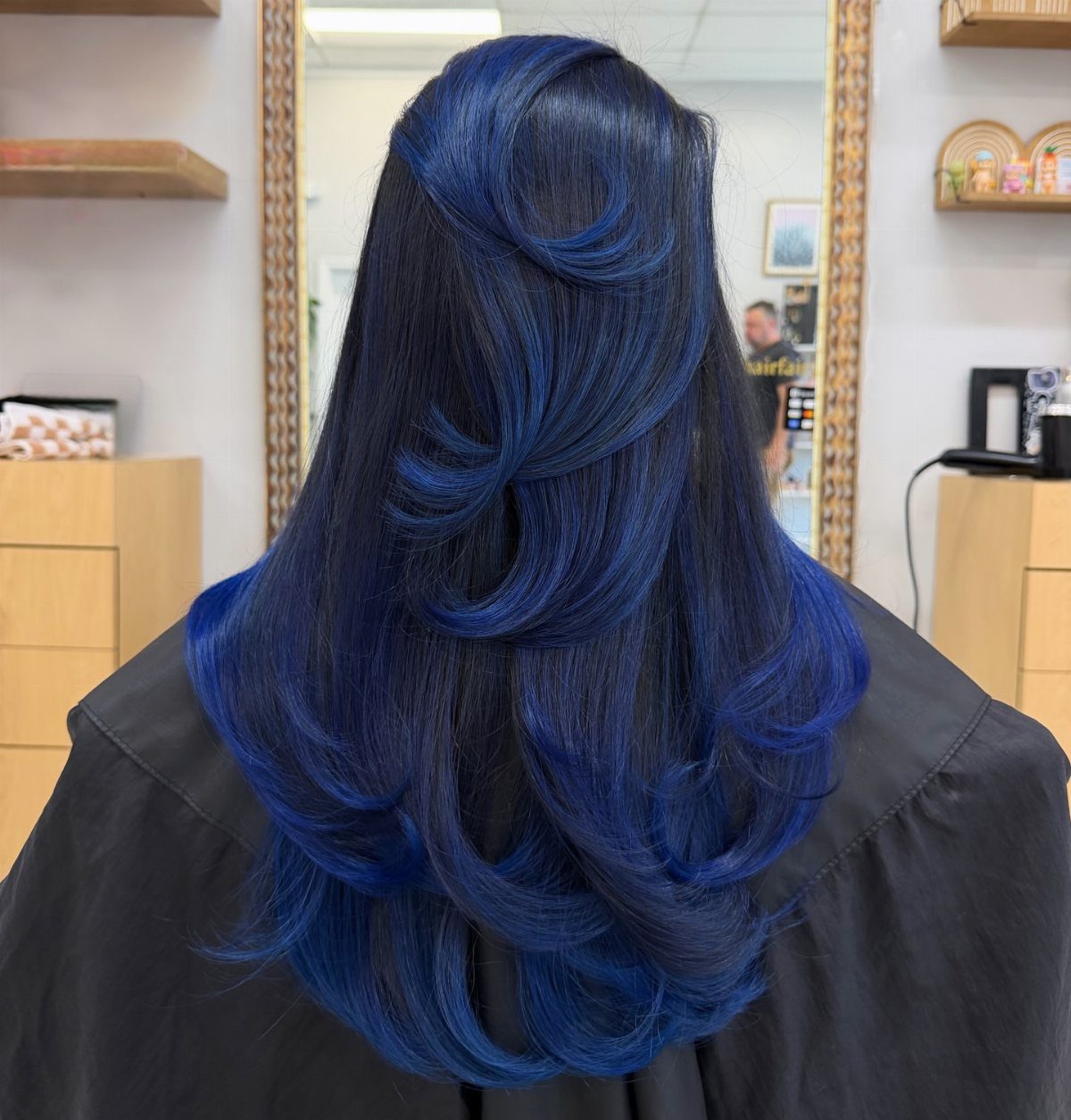 Long, layered deep blue-black hair styled in glossy curls at a salon