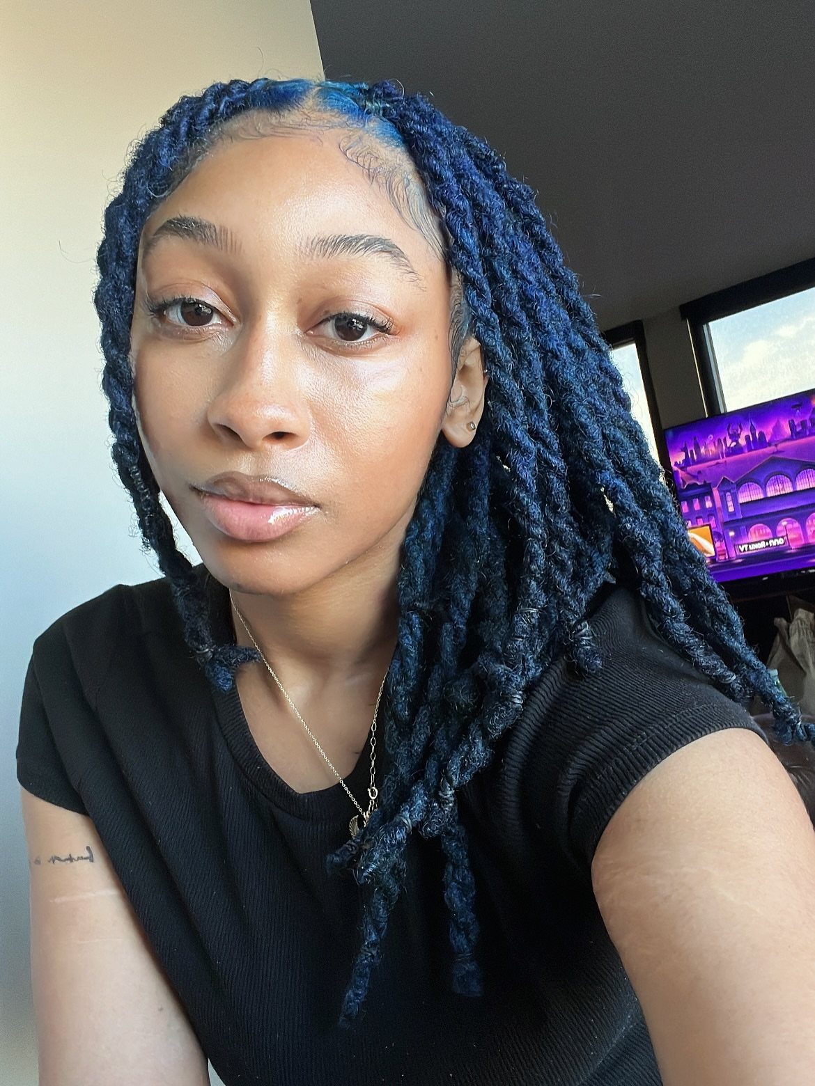 Long blue-black twists frame a person wearing a black shirt indoors