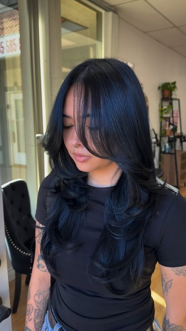 Long layered navy-blue hair with curled ends in a salon