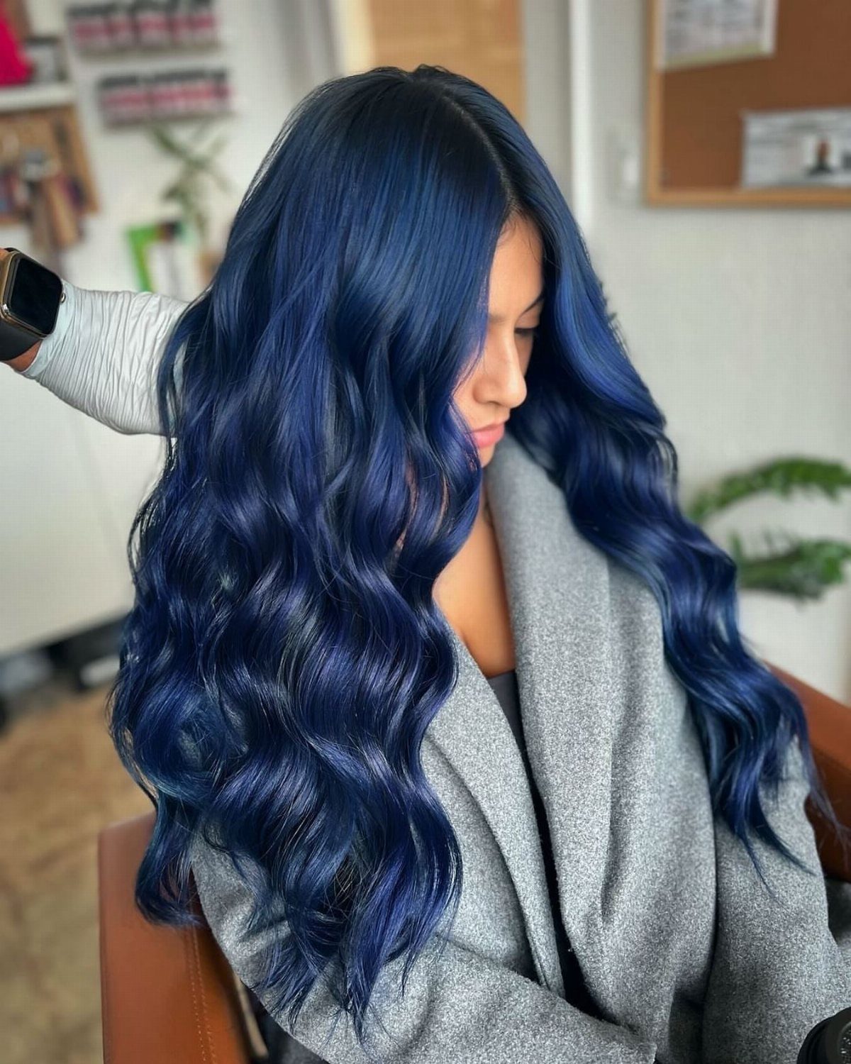 Long navy-blue waves cascade over a gray coat in a salon