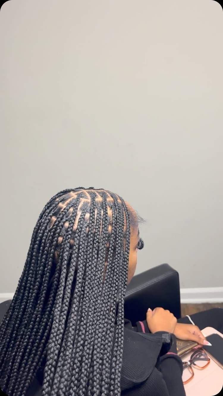 Long black box braids fall down the back of a seated person in a salon