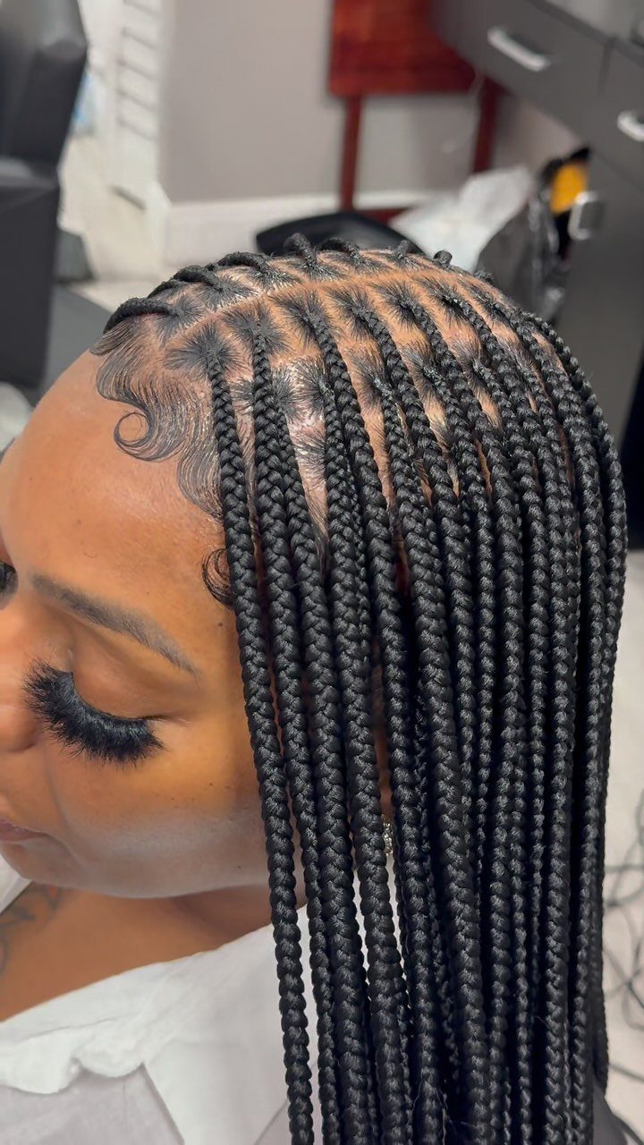Long, chunky black box braids fall over one shoulder in a salon