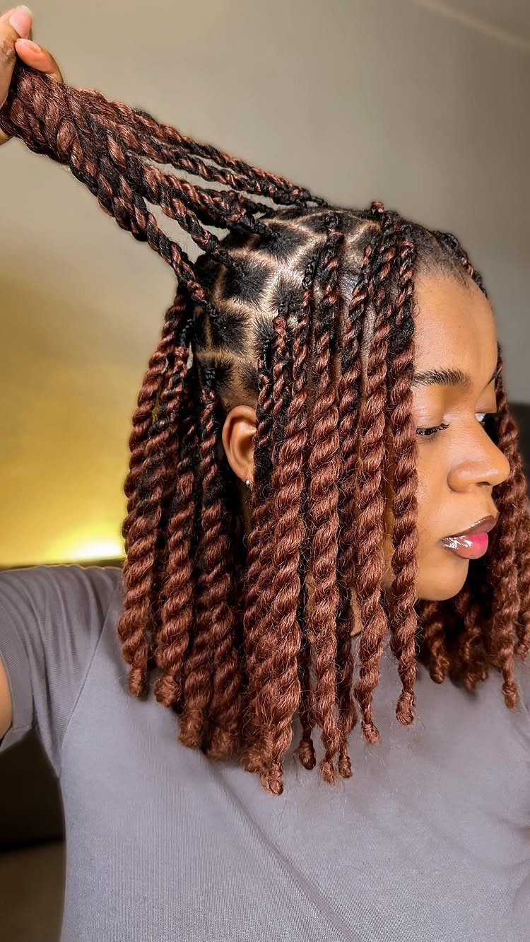 Woman lifting reddish-brown textured twists with geometric braids at the hairline