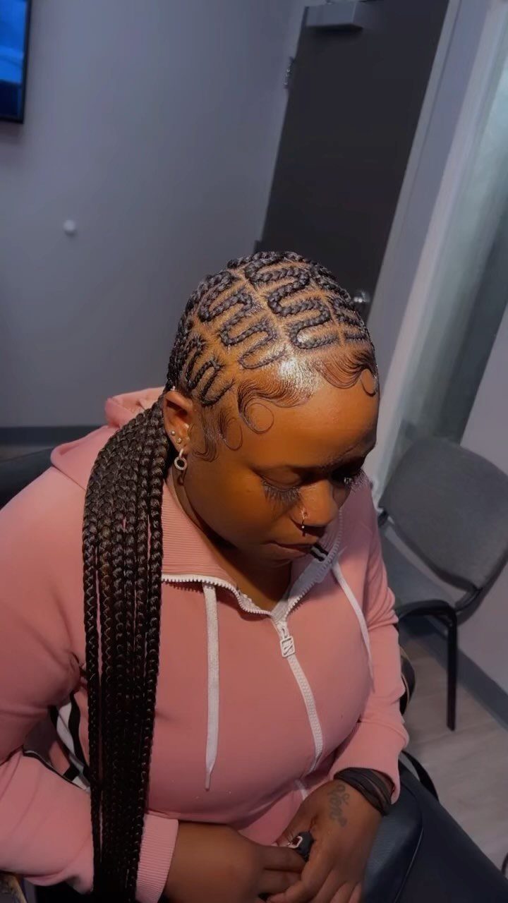 Curved scalp braids feed into long dark braids over a pink hoodie
