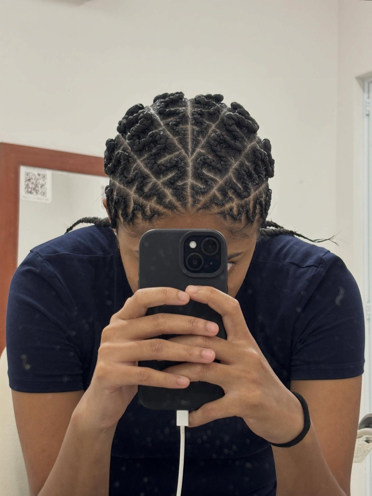 Person shows raised braids with zigzag partings while holding a phone