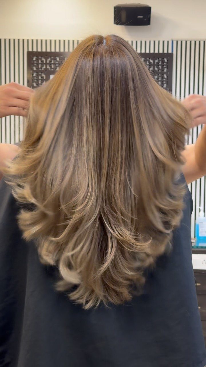 Long layered ash-brown hair with cool taupe highlights spread out in a salon