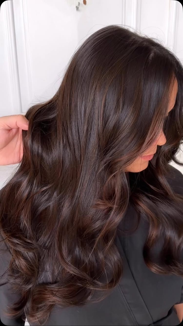 Glossy chocolate-brown hair falls in loose waves over a black top