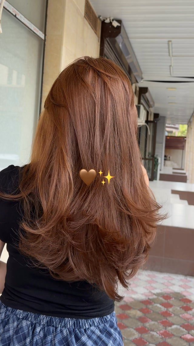 Layered cinnamon-brown hair falls in loose curls over a black top