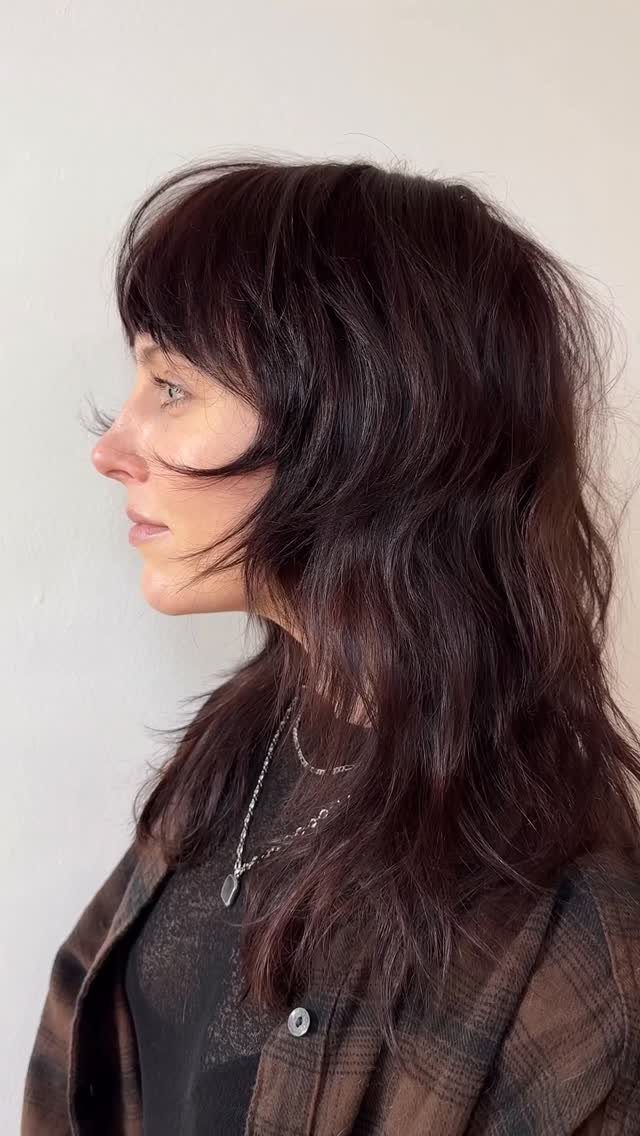 Woman displaying long wavy dark brown hair with bangs and subtle warm highlights