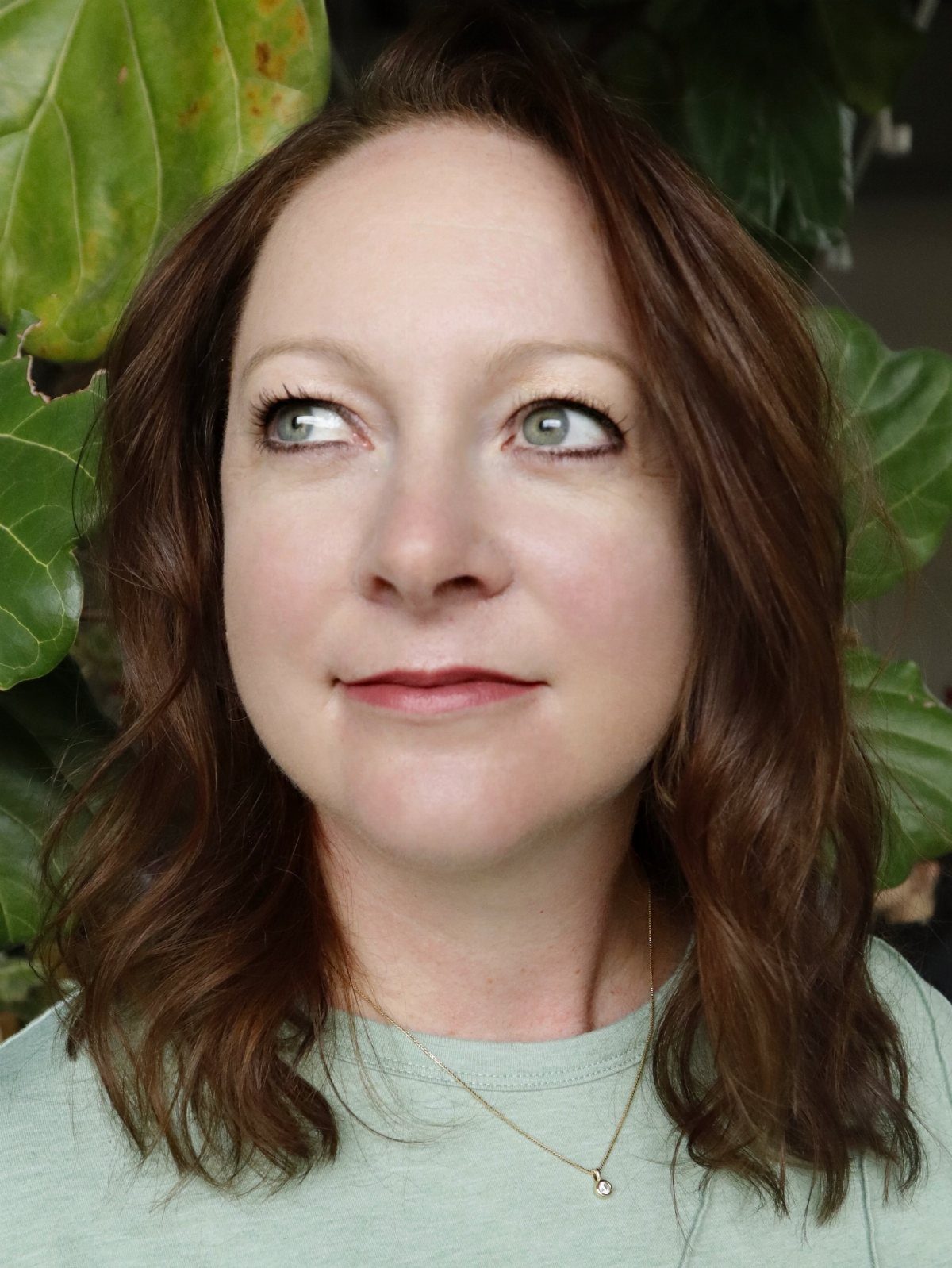 Woman with shoulder-length wavy light auburn-brown hair against green leaves