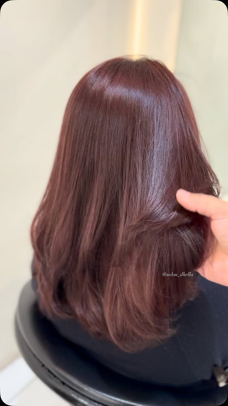 Glossy mahogany-brown hair falls in soft waves over a black salon cape
