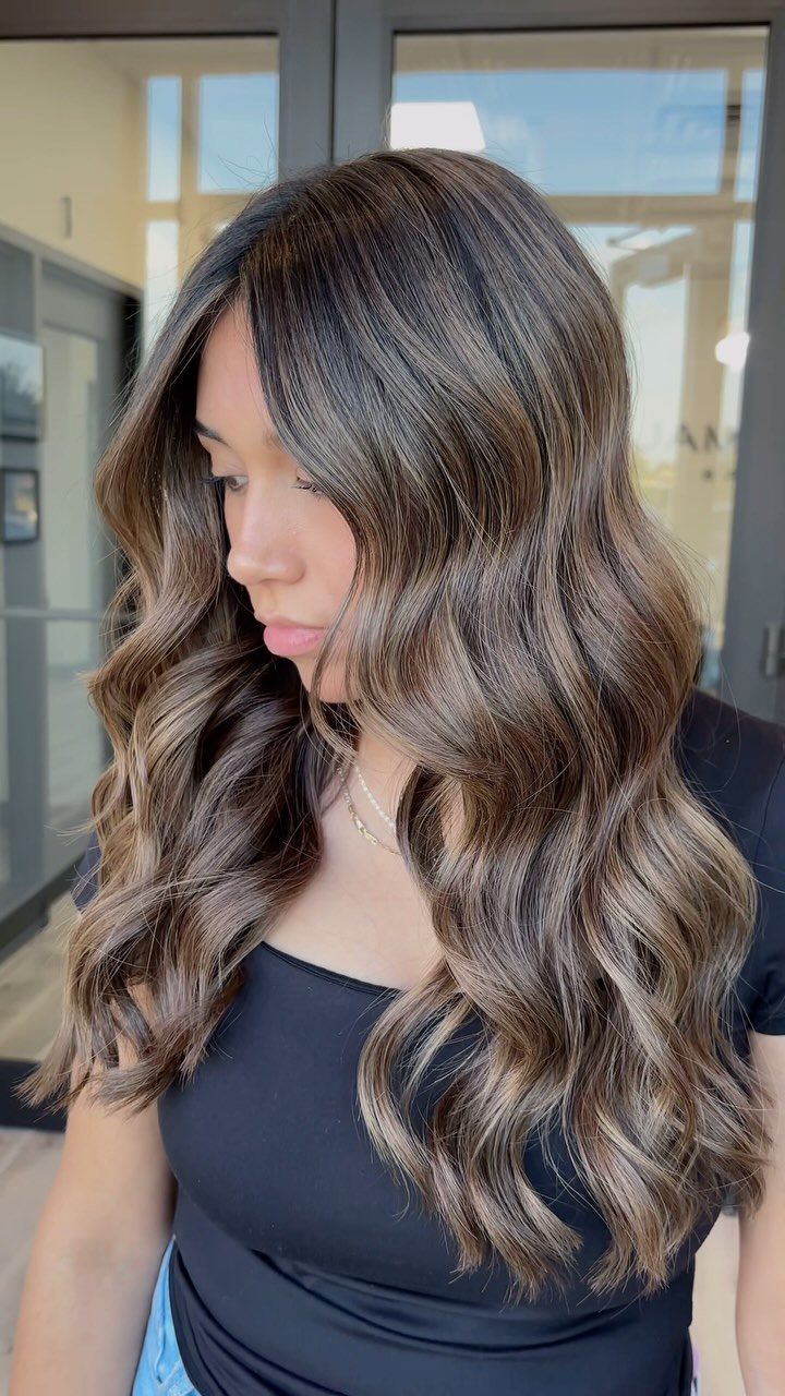 Woman with long, wavy mushroom brown hair and subtle taupe highlights