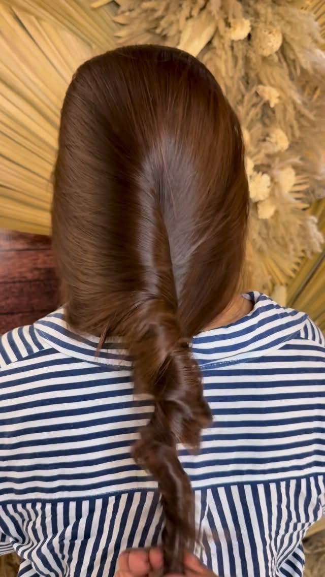 Dark brown hair styled into a long braid against beige dried grasses