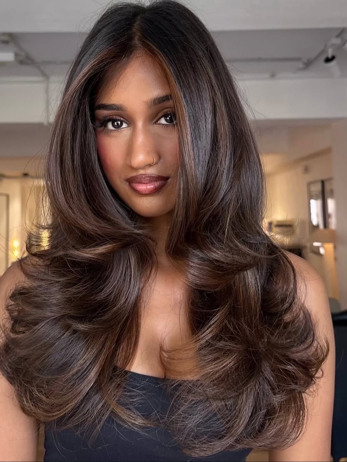 Woman with long, voluminous dark brown layered hair and softly curled ends