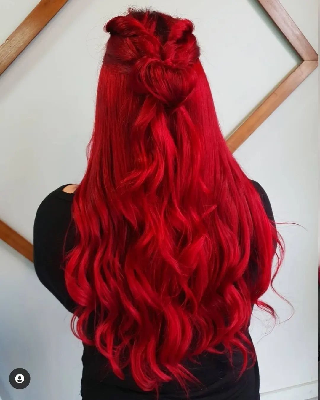 Long vivid red waves fall down a person's back beneath a twisted crown bun