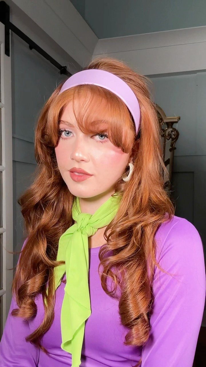 Person with curled reddish-orange layers, purple headband, and purple outfit