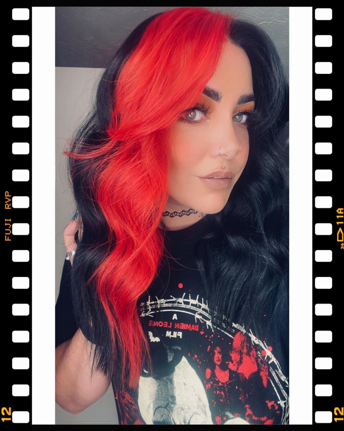 Person with long, wavy hair dyed vivid red on one side and black on the other