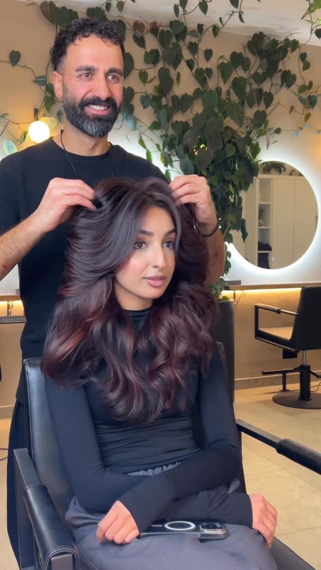 Woman with long dark cherry brown balayage hair being styled in a salon