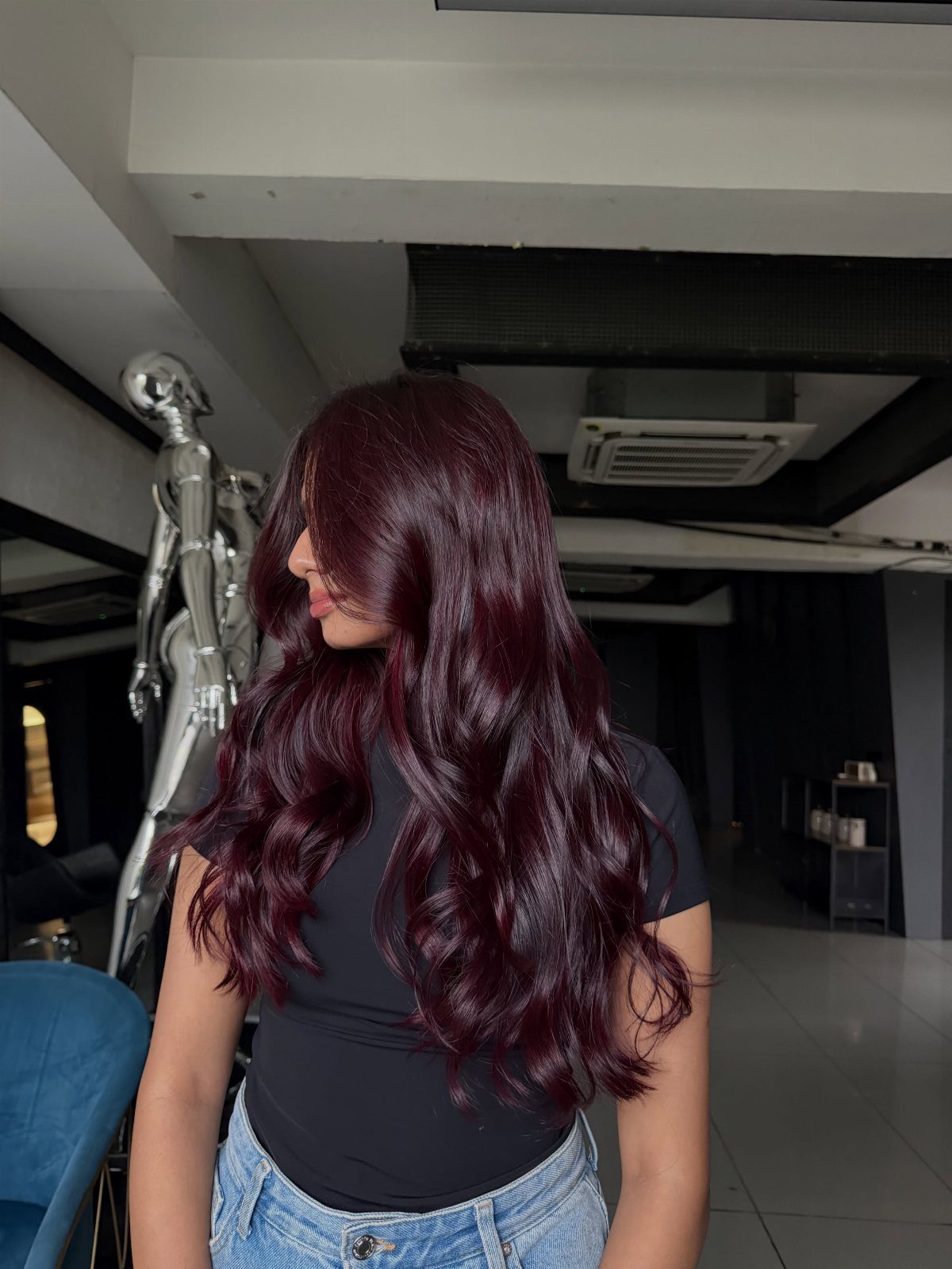 Long glossy burgundy-brown hair falls in waves over a black top