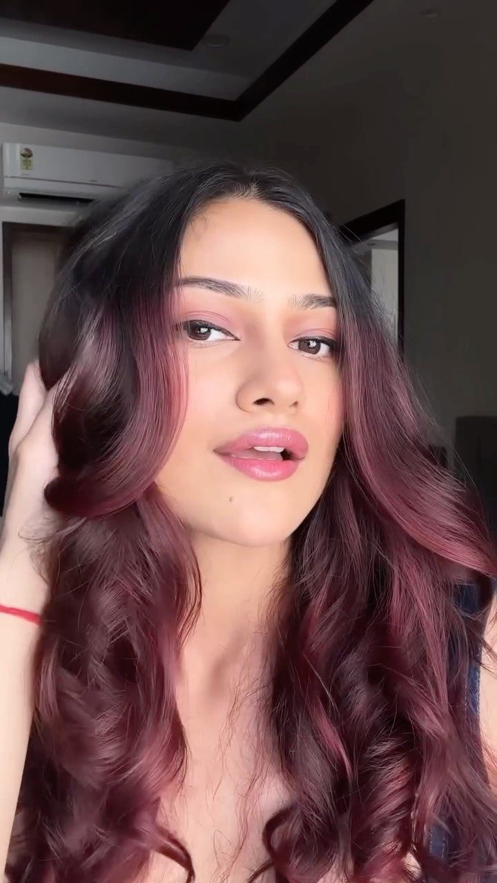Person showing long wavy burgundy-red hair with dark roots