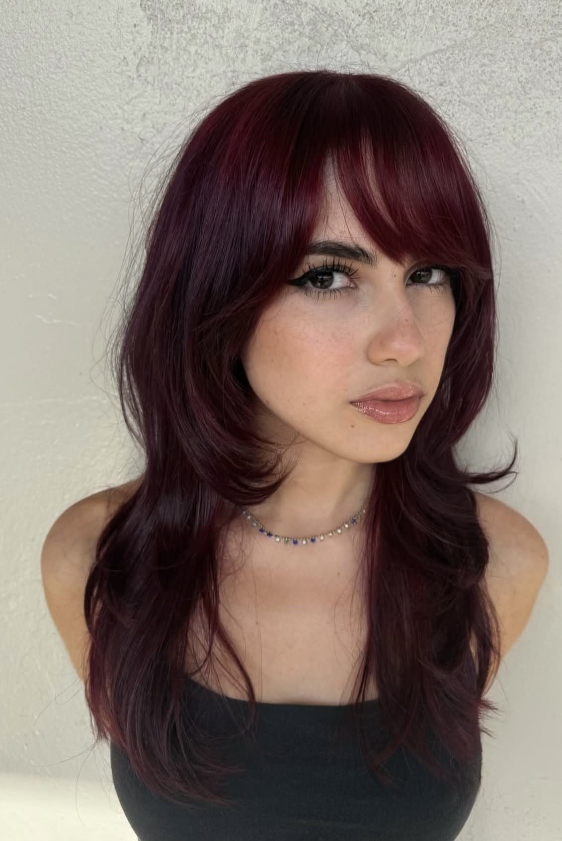 Woman showcasing long burgundy cherry cola hair with full bangs and layered waves
