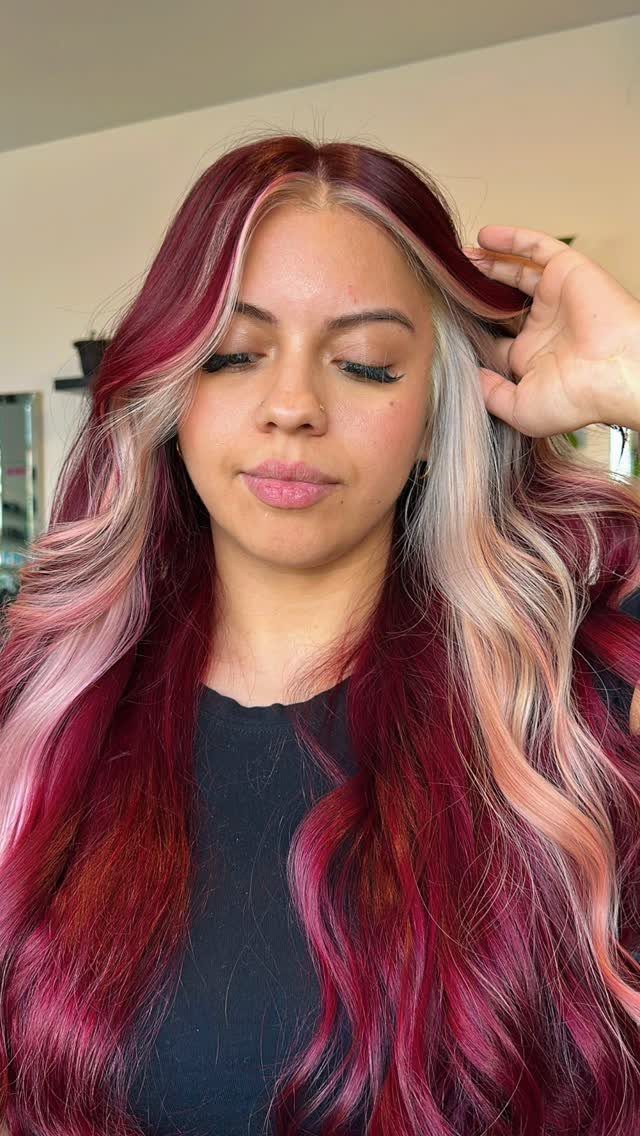 Woman showing long burgundy waves with pale pink and silver face-framing streaks