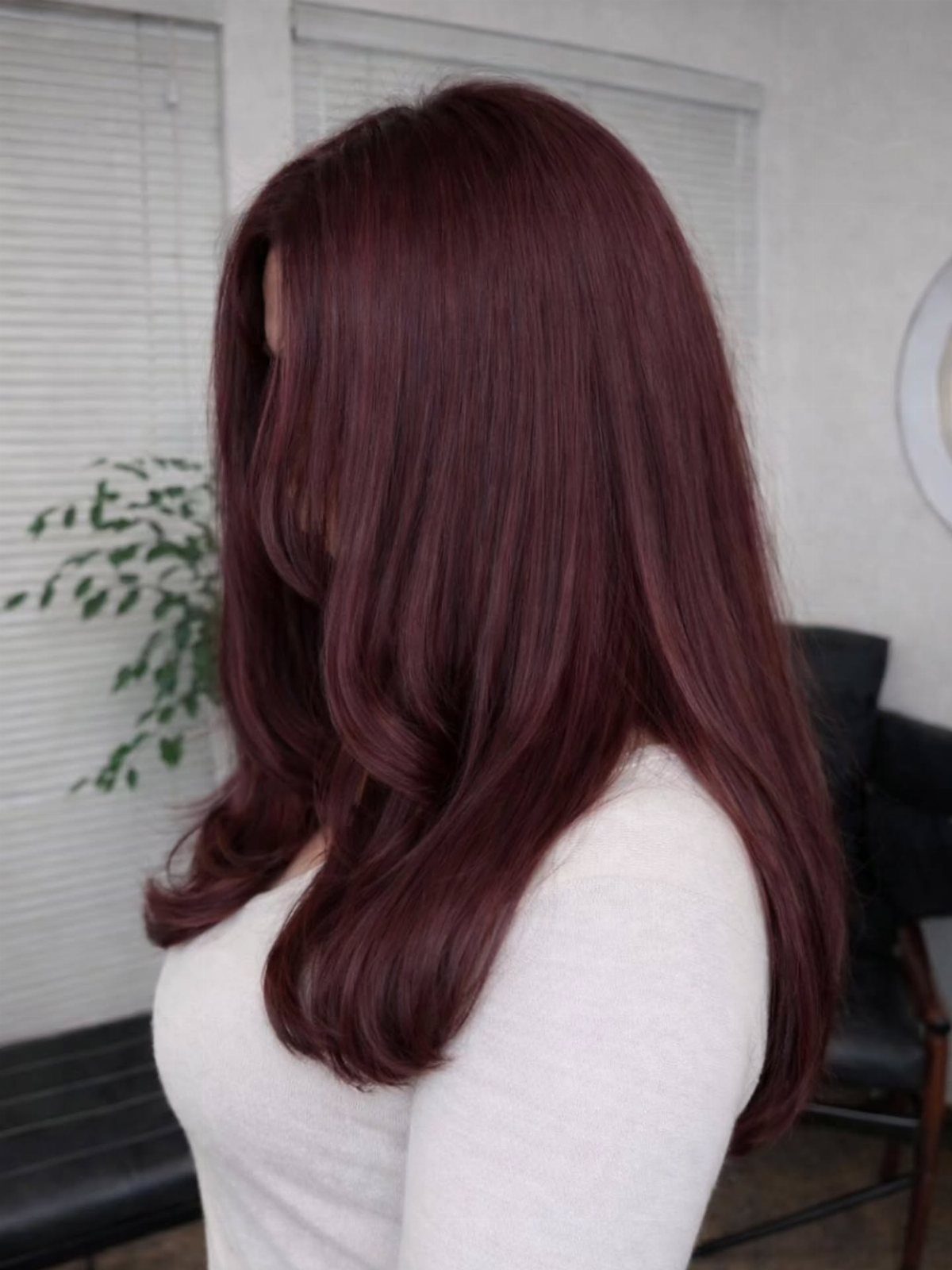 Long layered burgundy hair falls over a white top in soft curls